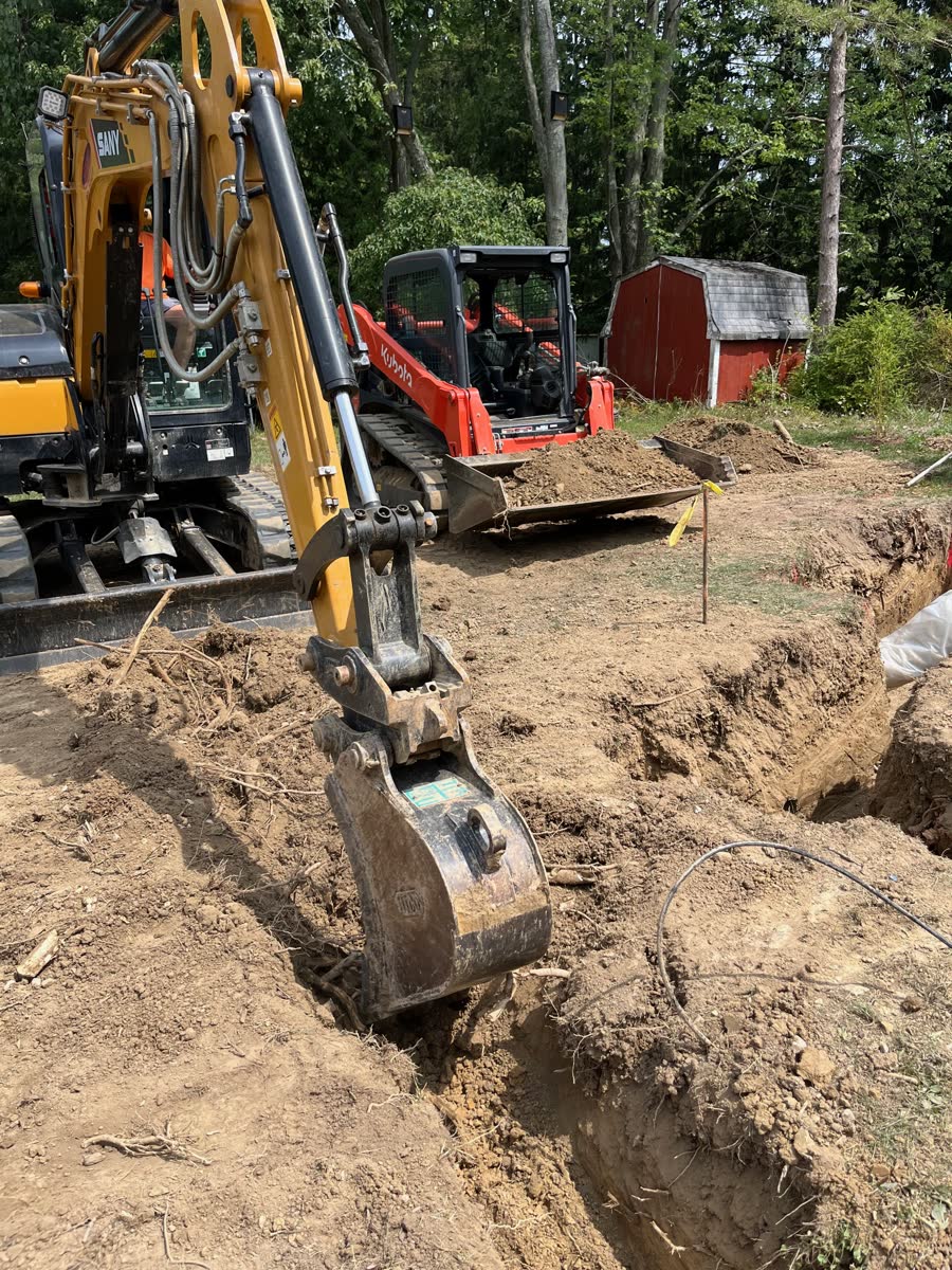 Excavator and skid steer digging a utility trench on a residential job site.