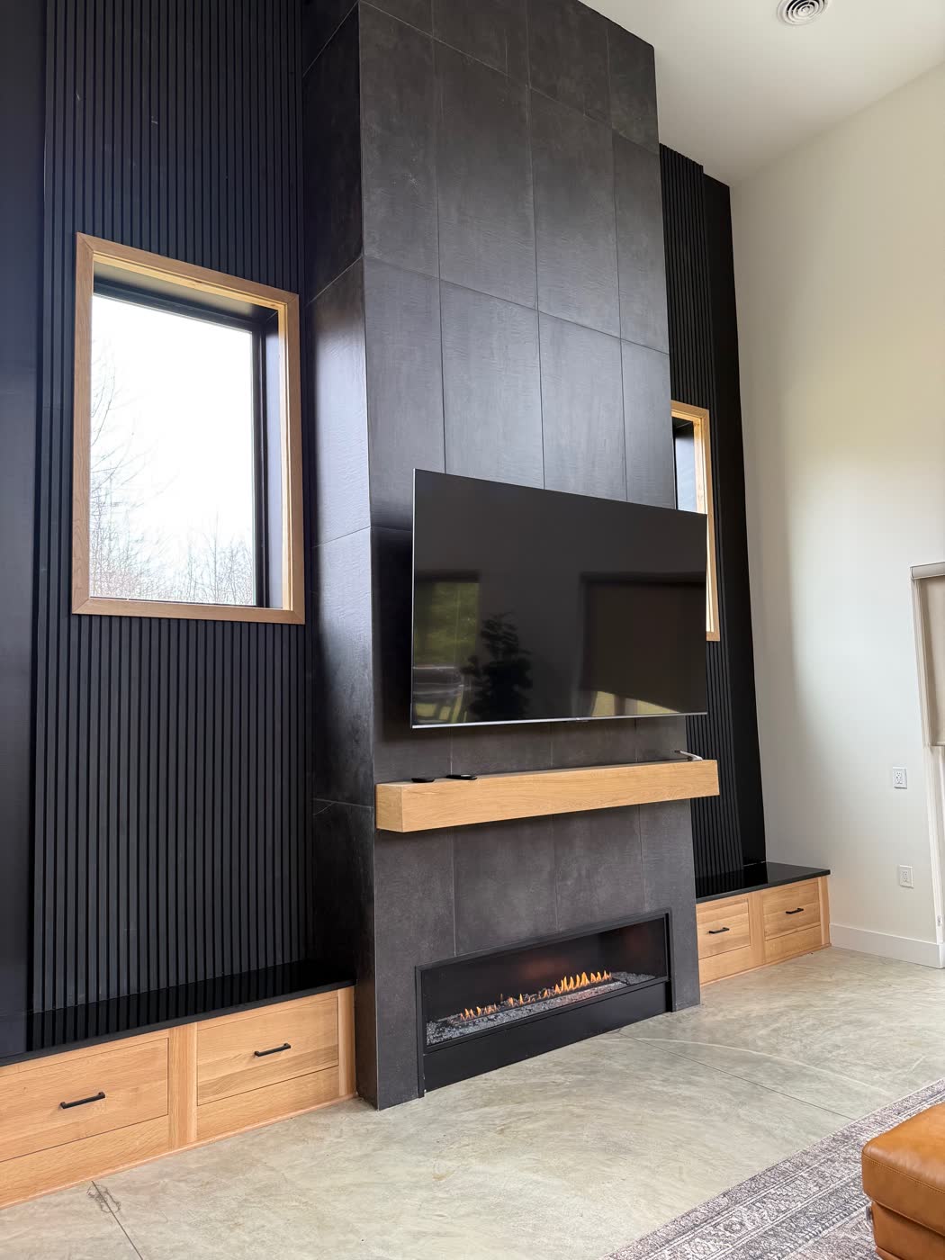 Living room feature wall with dark large-format tile, a linear gas fireplace, wall-mounted TV, and built-in wood cabinetry.