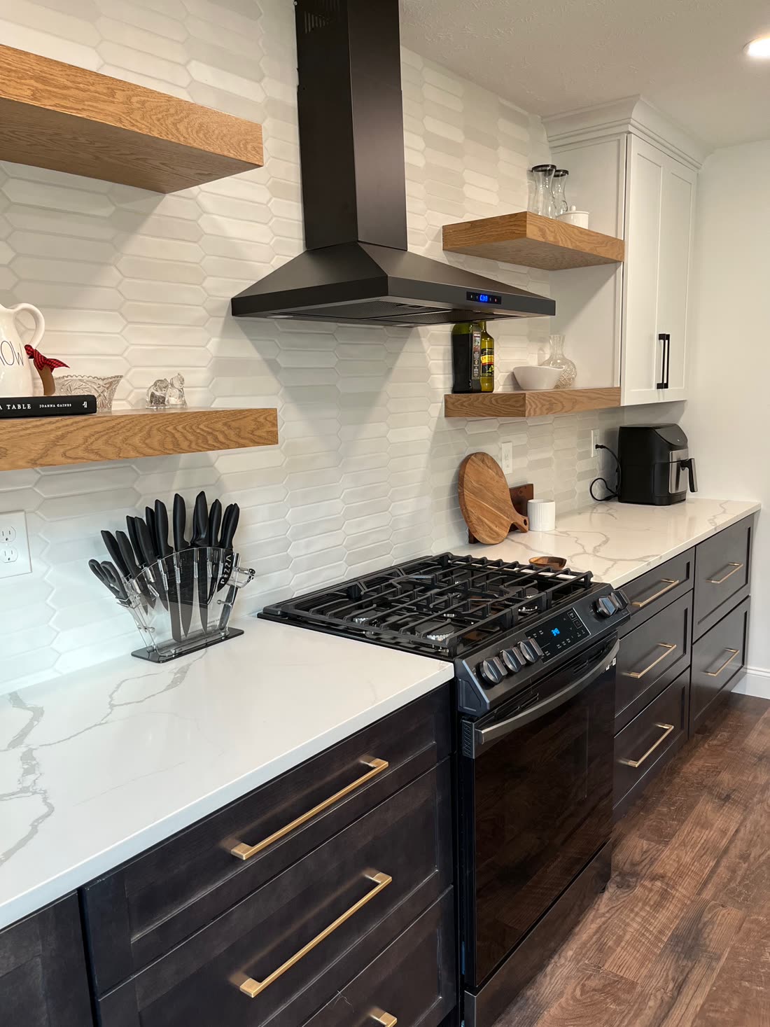 Remodeled kitchen with dark cabinetry, brass hardware, quartz countertops, and a black wall-mount range hood.
