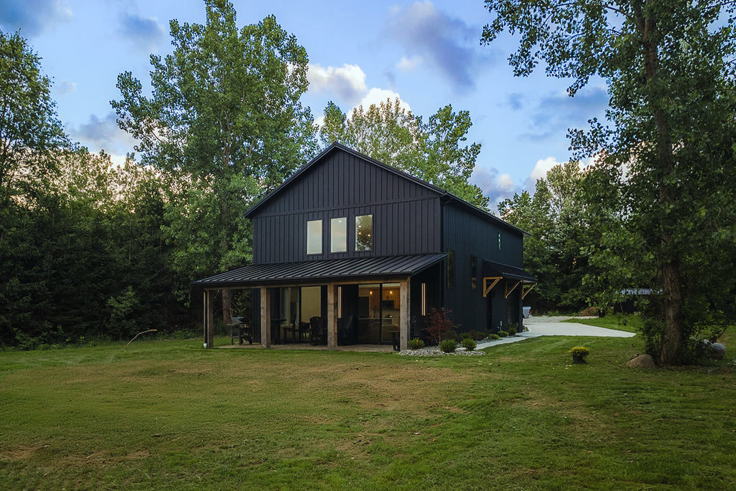 Dark barn-style home exterior at dusk with large windows and warm interior lighting.